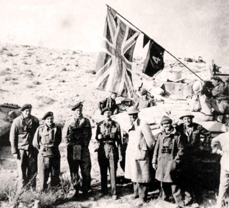The link-up at Ed Duda. From left to right: three Tank Corps officers unnamed, Brigadier A.C. Willison, Lt-Col S.F. Hartnell, a Tank Corps officer unnamed, and Captain E.D. Blundell.This flag flew on the fortress in Tobruk until the town fell to Rommel’s Afrika Korps on 21st June, 1942.
